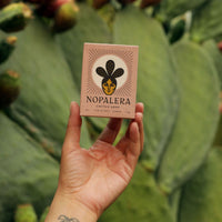 Hand holding Nopalera cactus soap in front of lush cactus greenery.