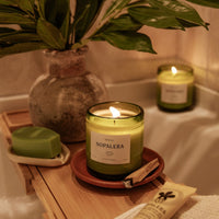 lit Nopalera Mérida scented candle in green glass jar on wooden bath tray