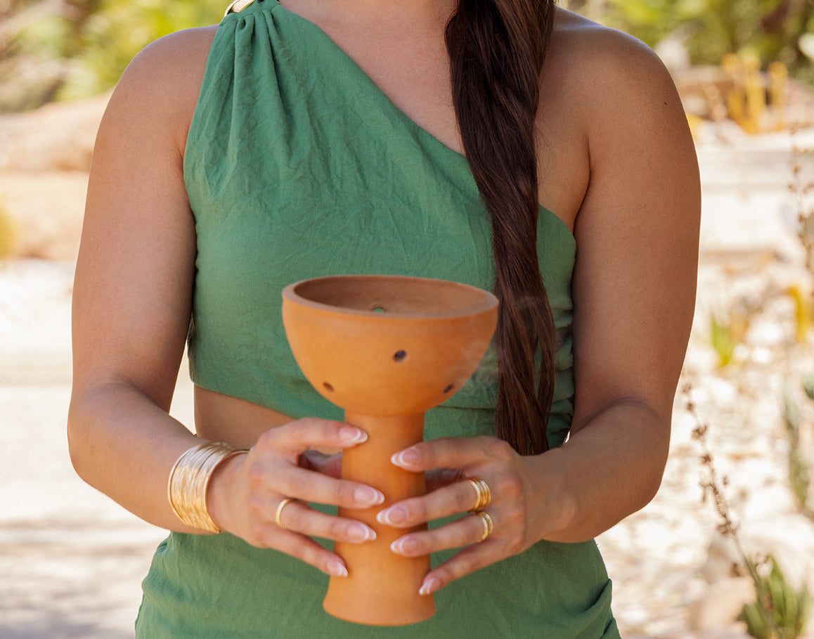 Person holding a handcrafted clay cup outdoors in a sunlit setting.