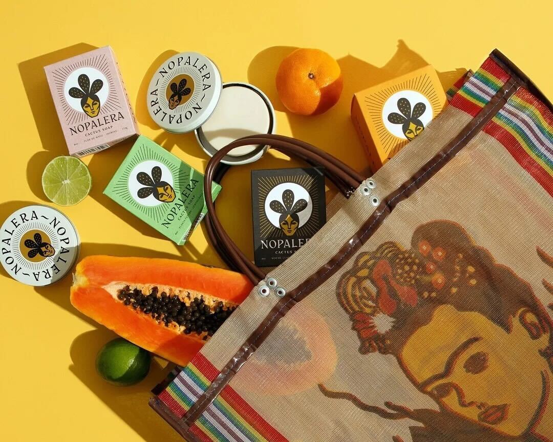 Nopalera self-care essentials with Citrus Lotion Bar, Lemongrass Soap, skincare products, fresh fruit, and Frida Kahlo-inspired travel pouch.