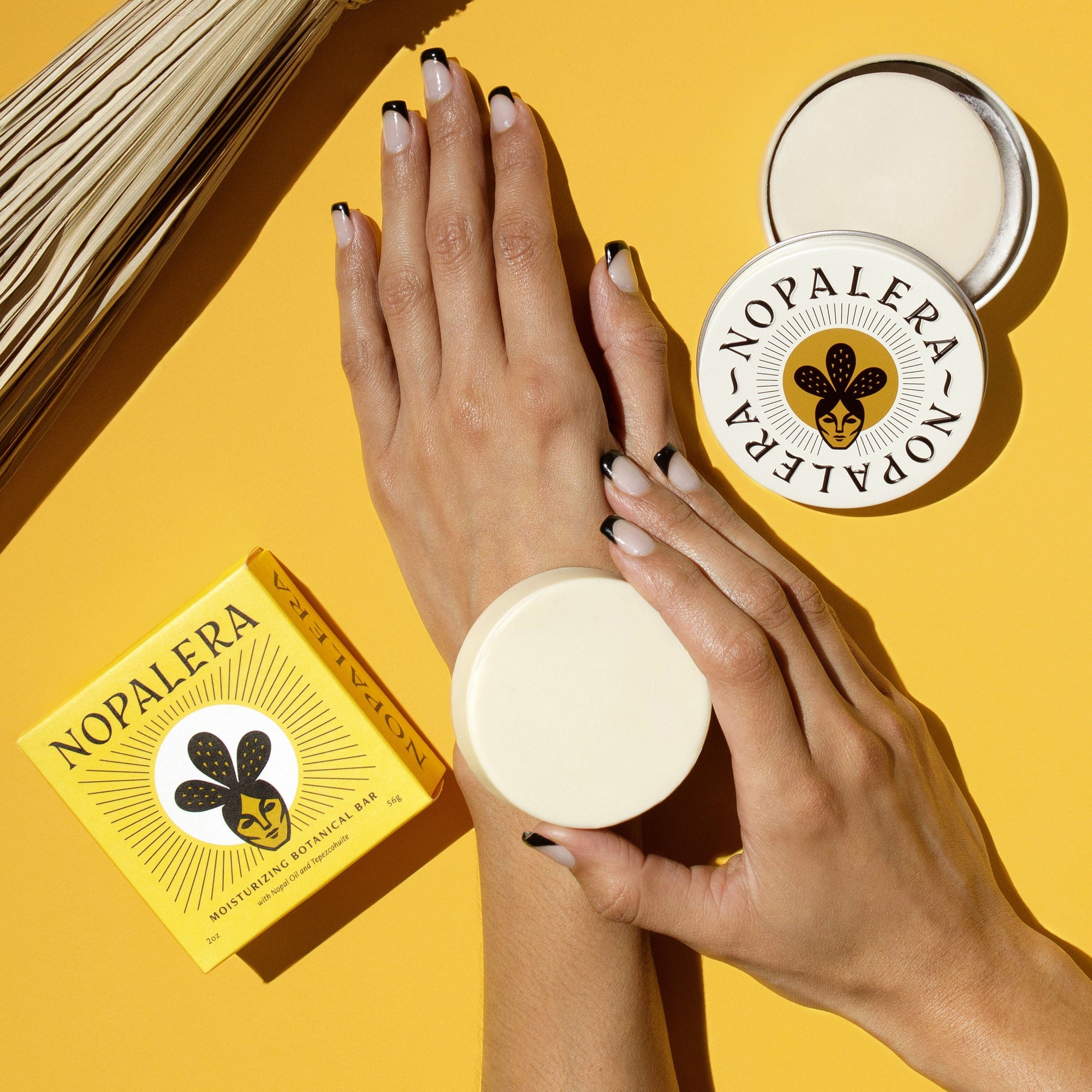Hands holding Nopalera citrus lotion bar against a bright yellow background.
