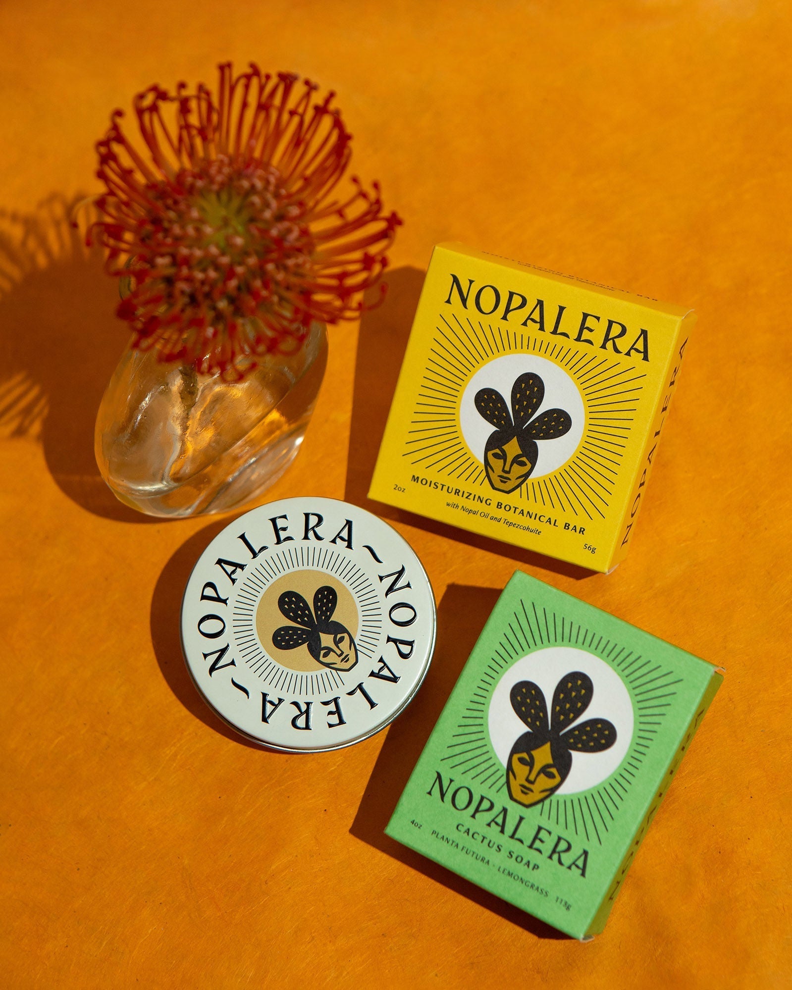 Nopalera Citrus Lotion Bar and Lemongrass Soap displayed with floral accents on a vibrant orange background.