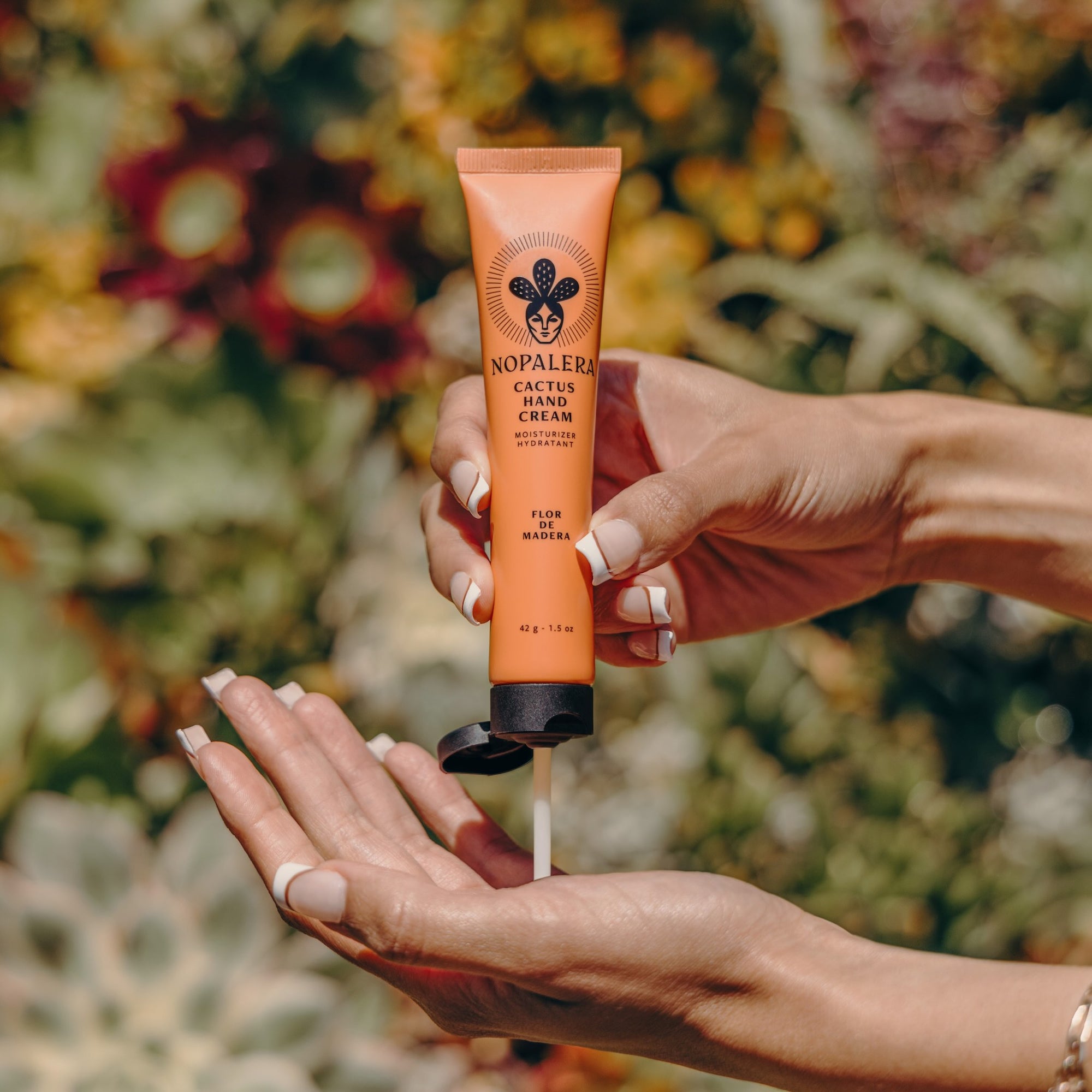 Hand applying Flor de Madera cactus hand cream with a floral background