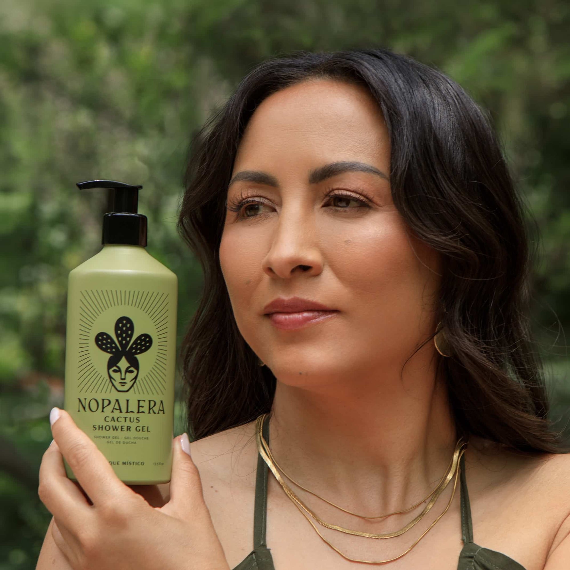 A woman holding a bottle of Nopalera Cactus Shower Gel against a blurred green outdoor background.
