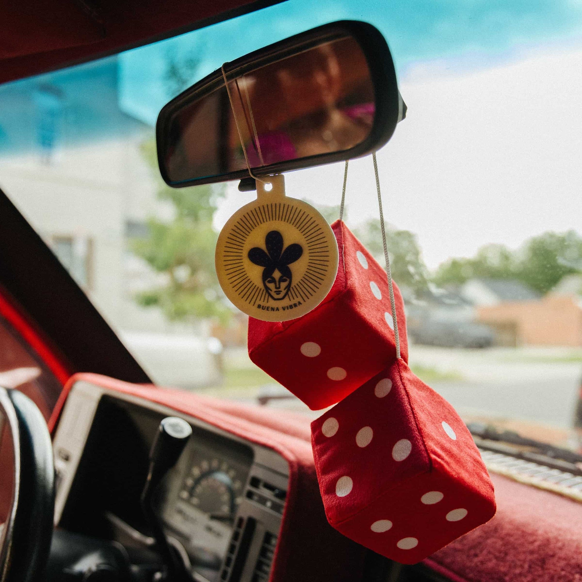 Buena Vibra car freshener hanging from a rearview mirror