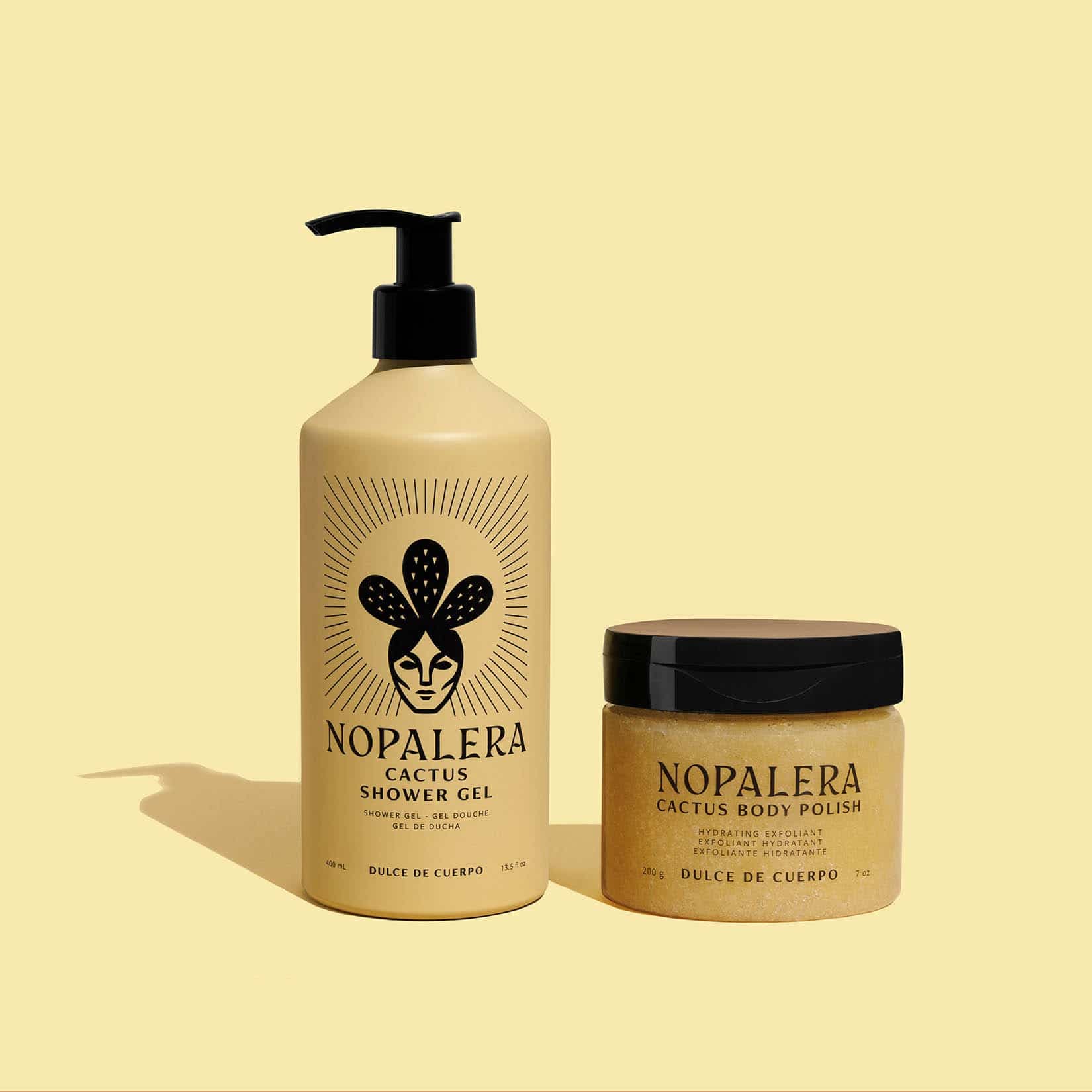Nopalera Cactus Shower Gel and Cactus Body Polish set on a pale yellow background. The shower gel is in a tall beige pump bottle with a black cap, and the body polish is in a matching beige jar with a black lid.