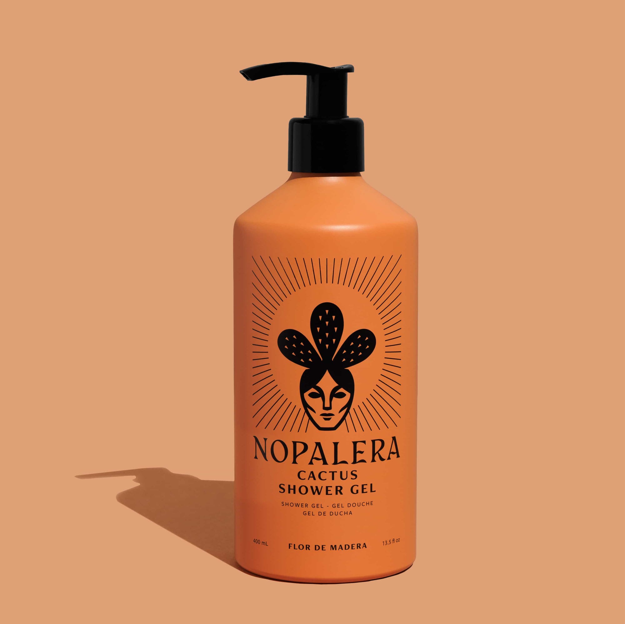 An orange pump bottle of Nopalera Cactus Shower Gel with a black pump dispenser, set against a solid peach-colored background with a soft shadow cast to the left.