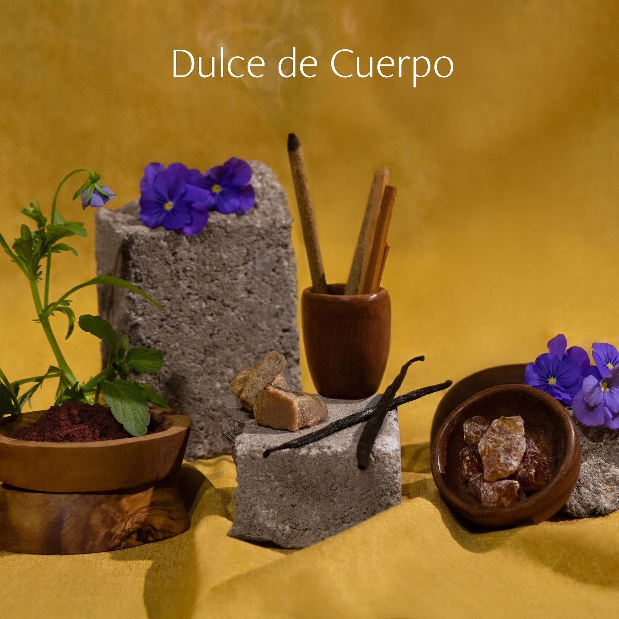 Dulce de Cuerpo fragrance ingredients including vanilla, incense, and flowers arranged in a warm golden composition