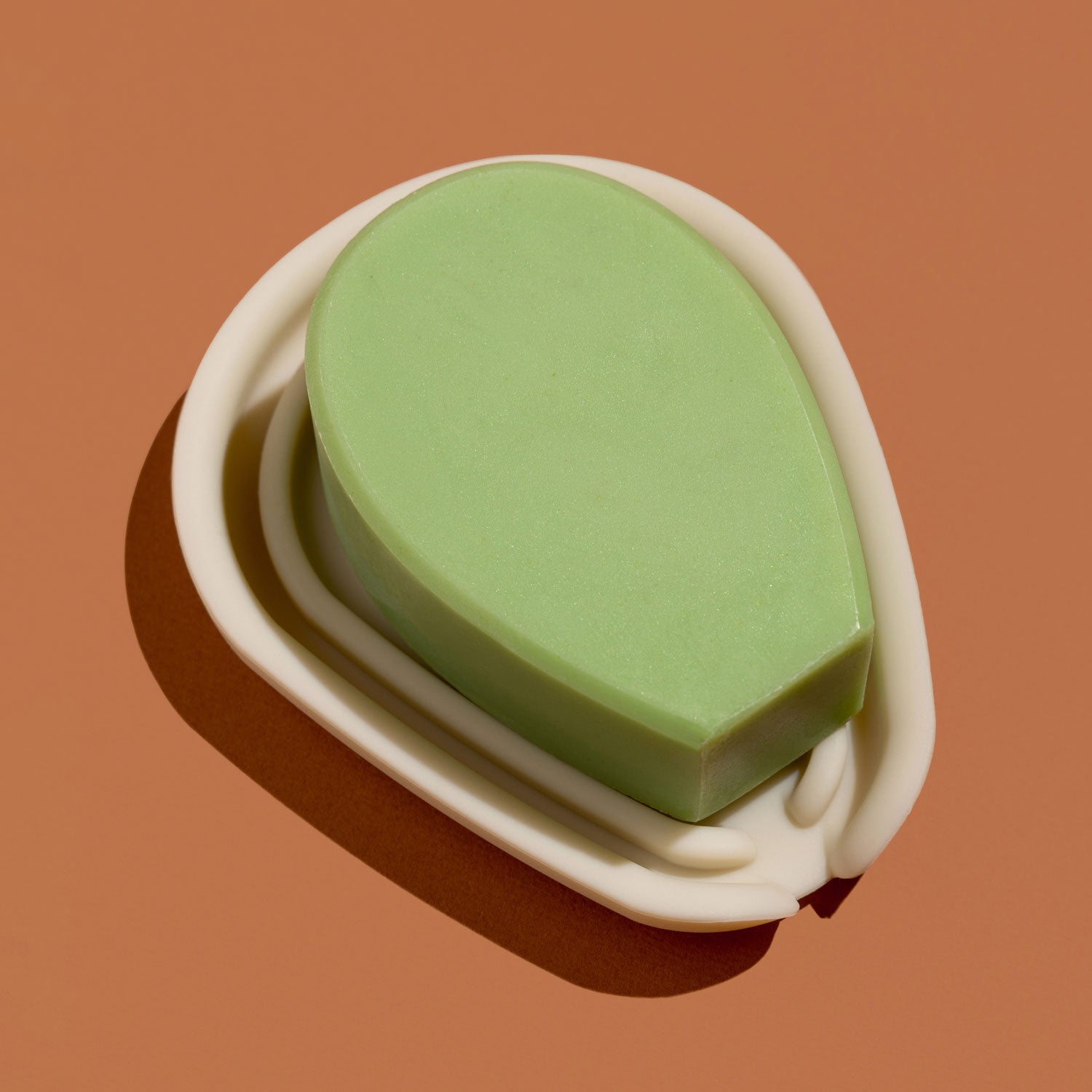 A green cactus-shaped bar of soap resting in a white silicone soap dish against a brown background.