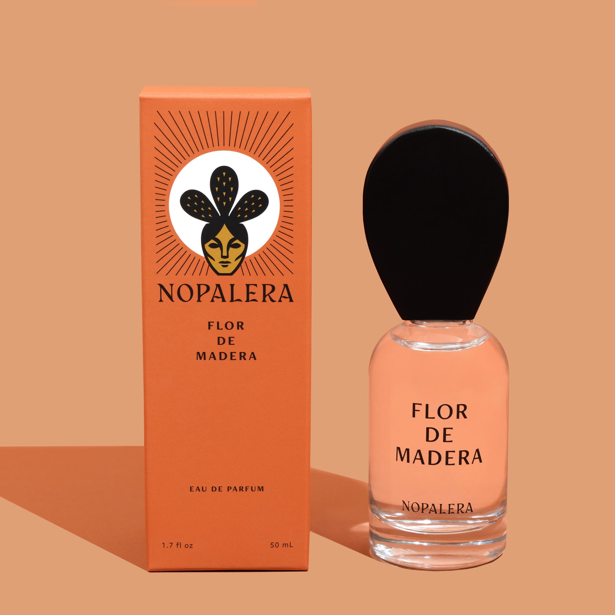 A glass of a 50ml Luxury Mexican fragrance  bottle of Flor de Madera perfume with a wooden cap, alongside its orange packaging box with the brand name Nopalera and product title.