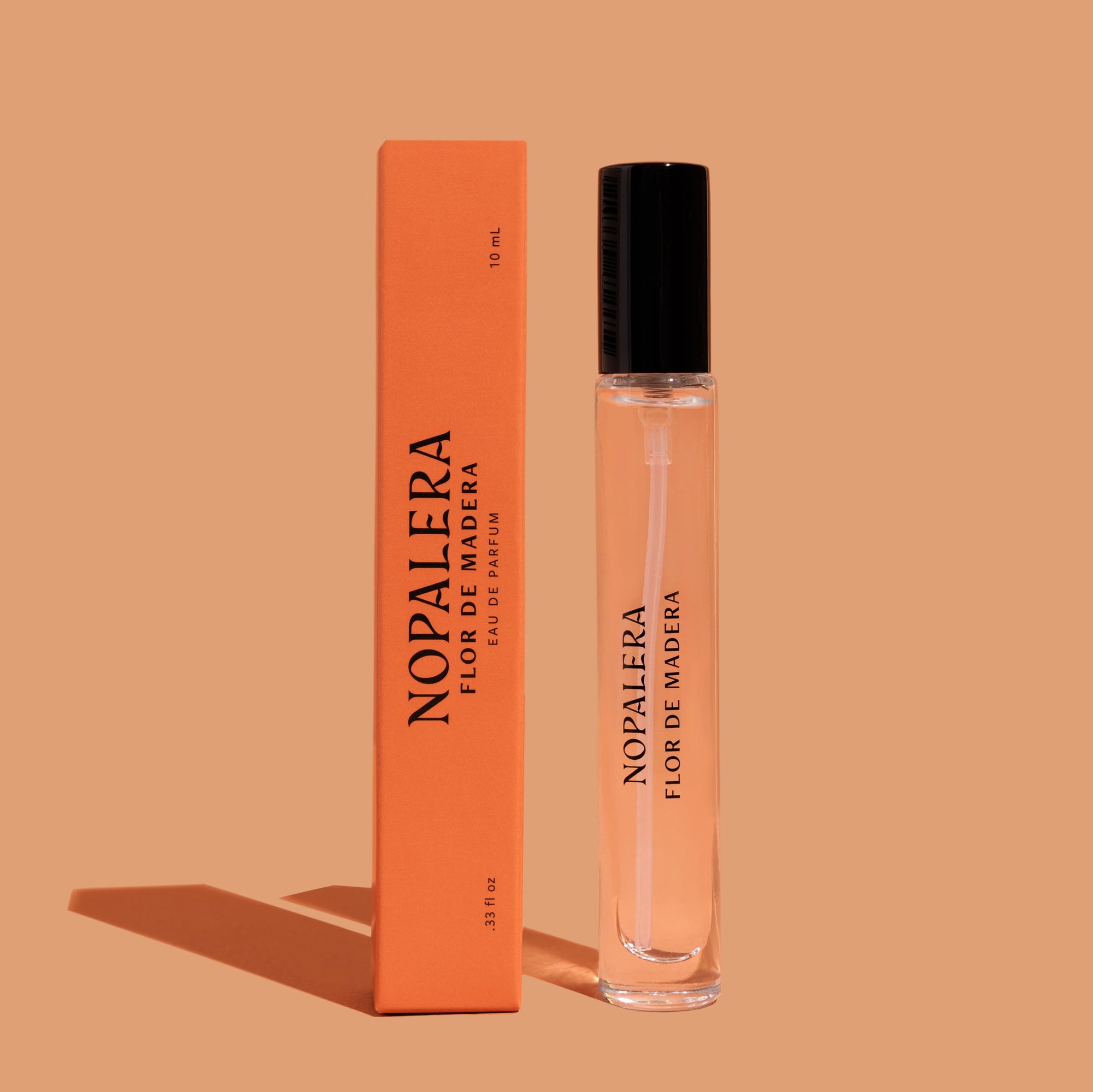 A 10mL Luxury Mexican fragrance travel spray bottle of Flor de Madera perfume next to its orange packaging box, both with the brand name 'Nopalera' printed on them.