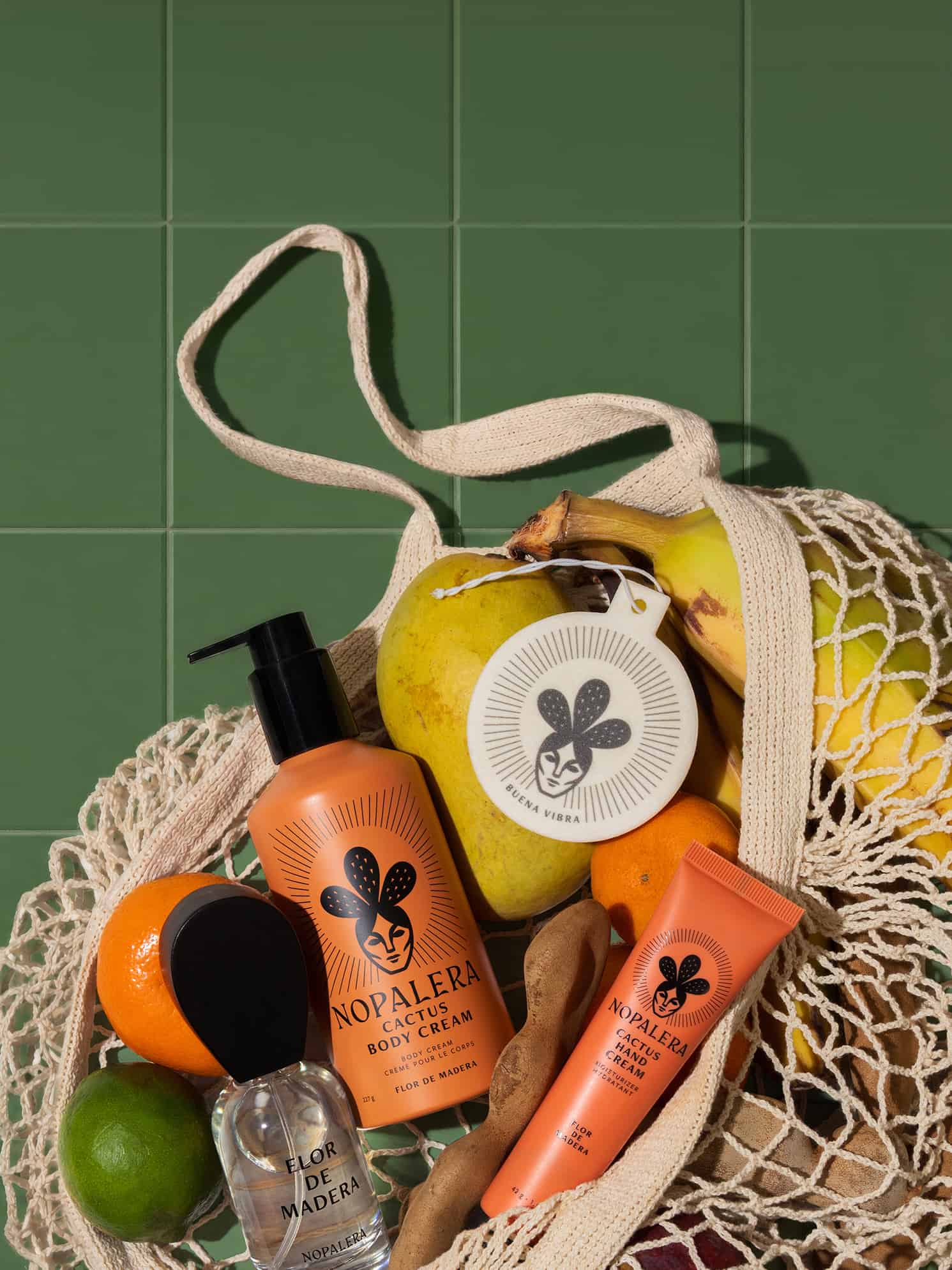 Nopalera skincare products in a mesh bag with fruits on a green tiled background