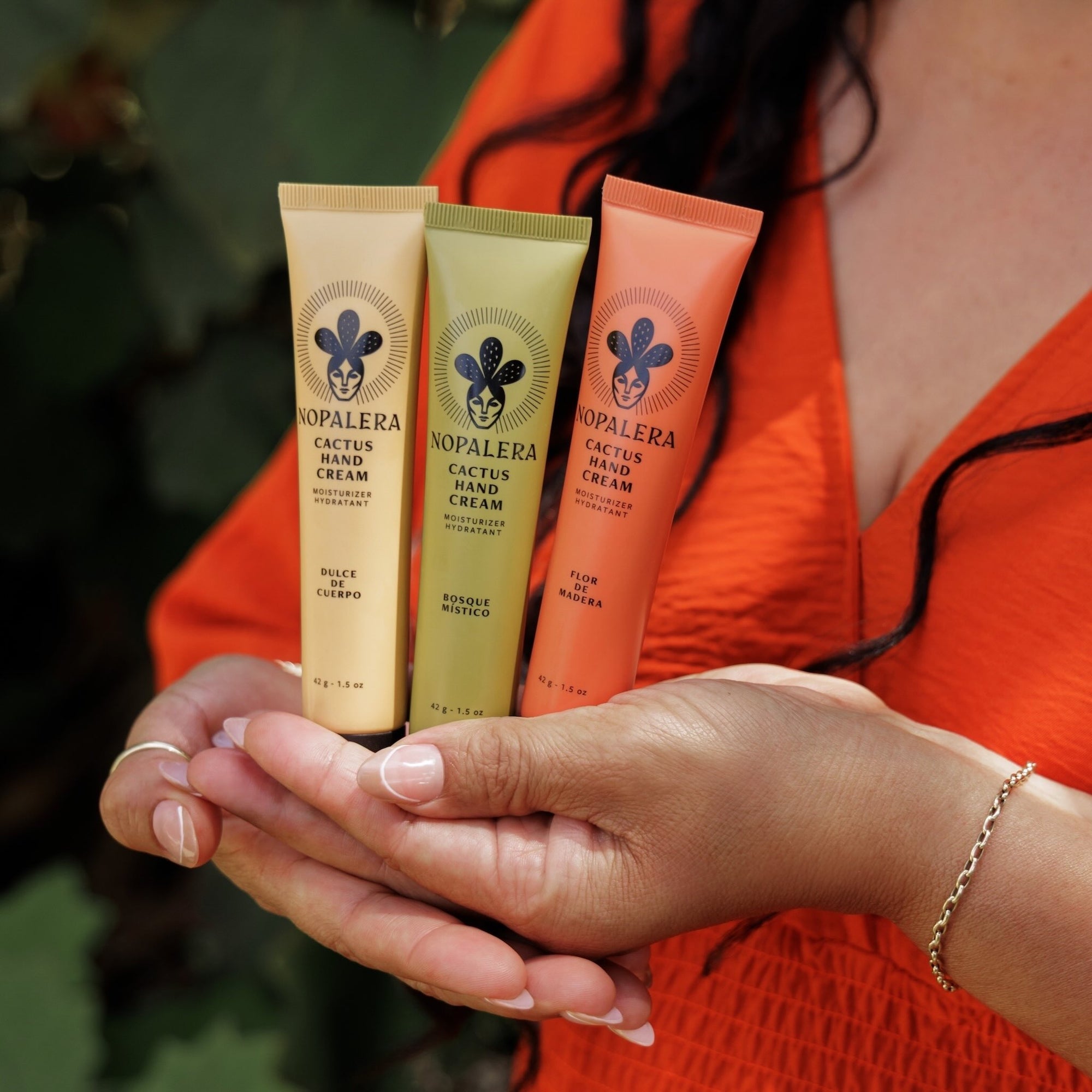 Three Nopalera cactus hand cream tubes held in a person's hands with a blurred background.