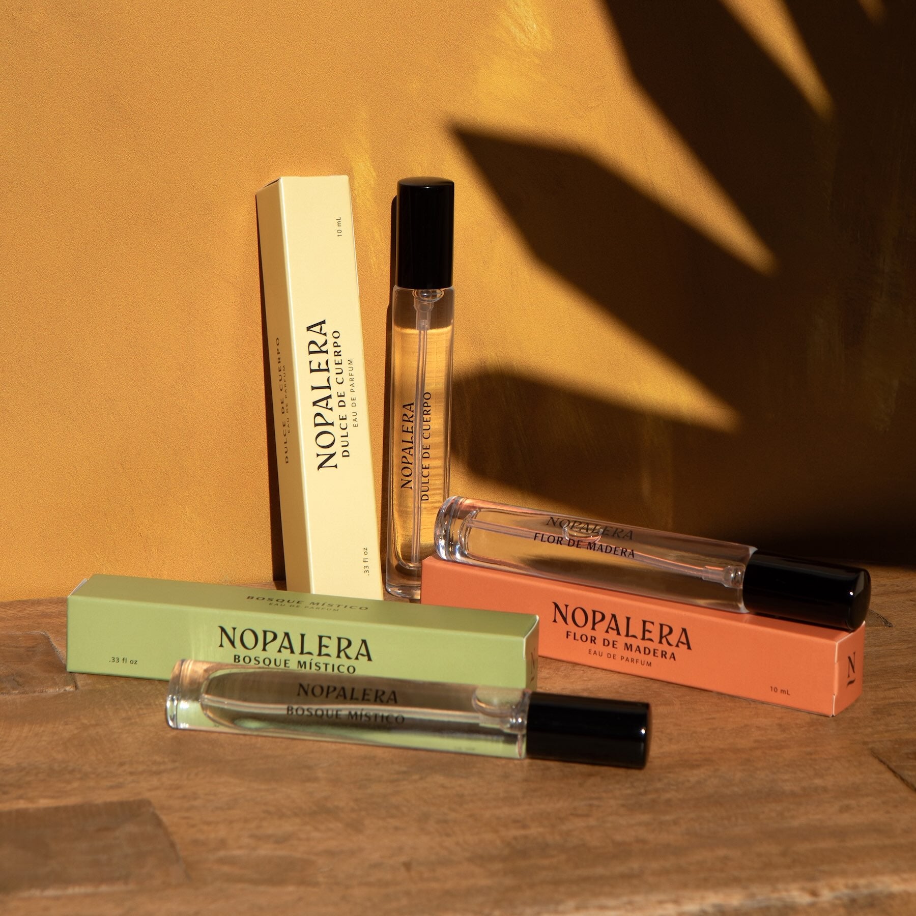 Nopalera travel perfume rollers in Dulce de Cuerpo, Flor de Madera, and Bosque Místico fragrances displayed with their boxes on a warm background