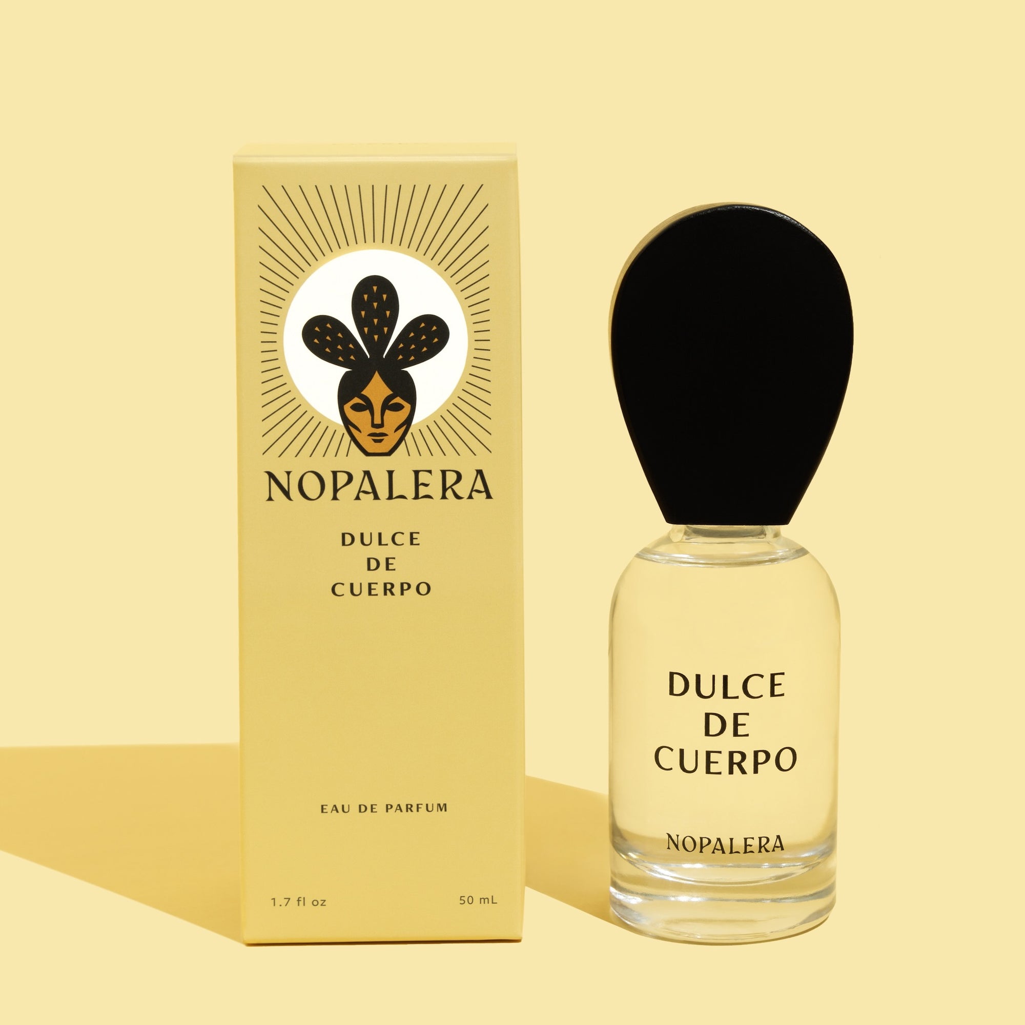 A glass bottle of 'Dulce de Cuerpo' luxury Mexican perfume with a wooden cap, placed next to its yellow packaging box with the Nopalerña brand logo.