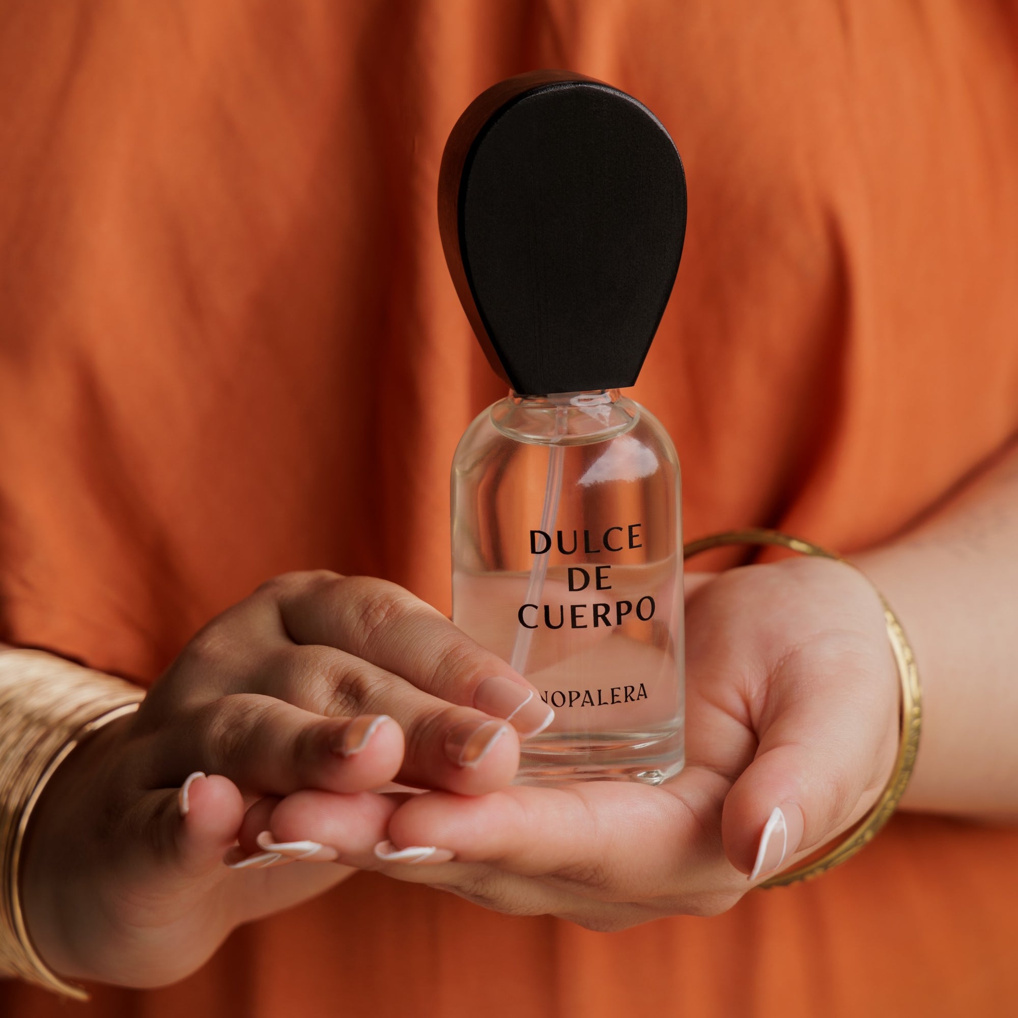 Hands holding Nopalera Dulce de Cuerpo luxury Mexican perfume bottle with wooden cap 
