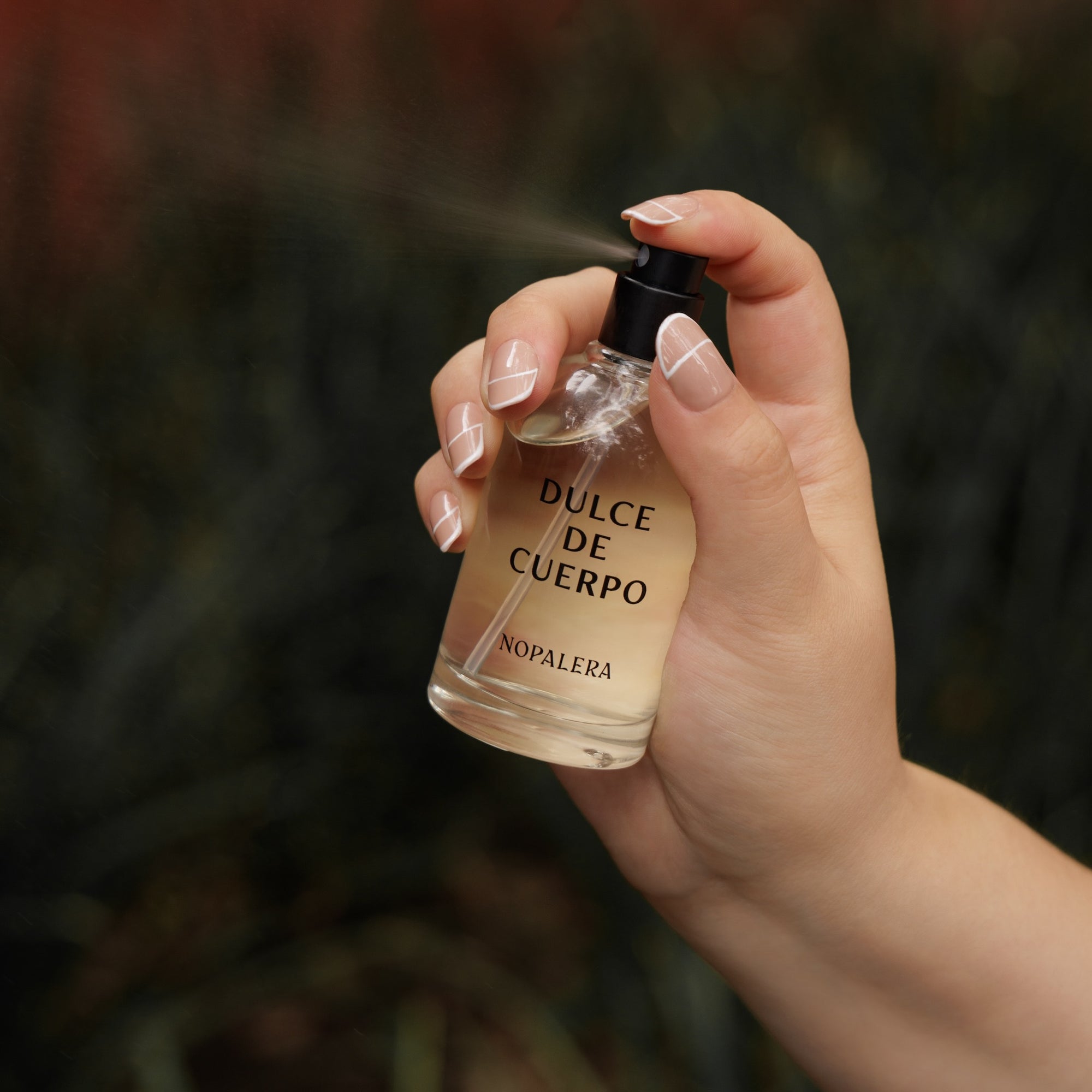 Hand spraying Nopalera Dulce de Cuerpo perfume from glass fragrance bottle.