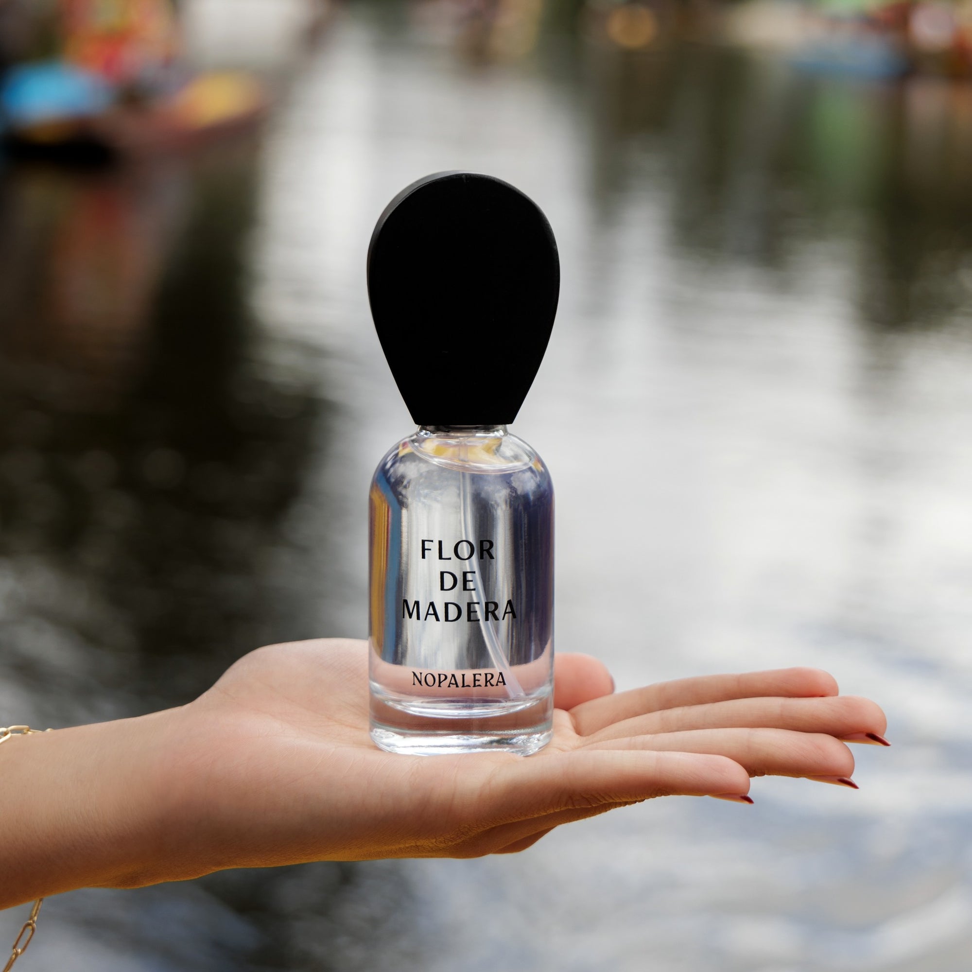 Hand holding Nopalera Luxury Mexican fragrance Flor de Madera perfume bottle with water background
