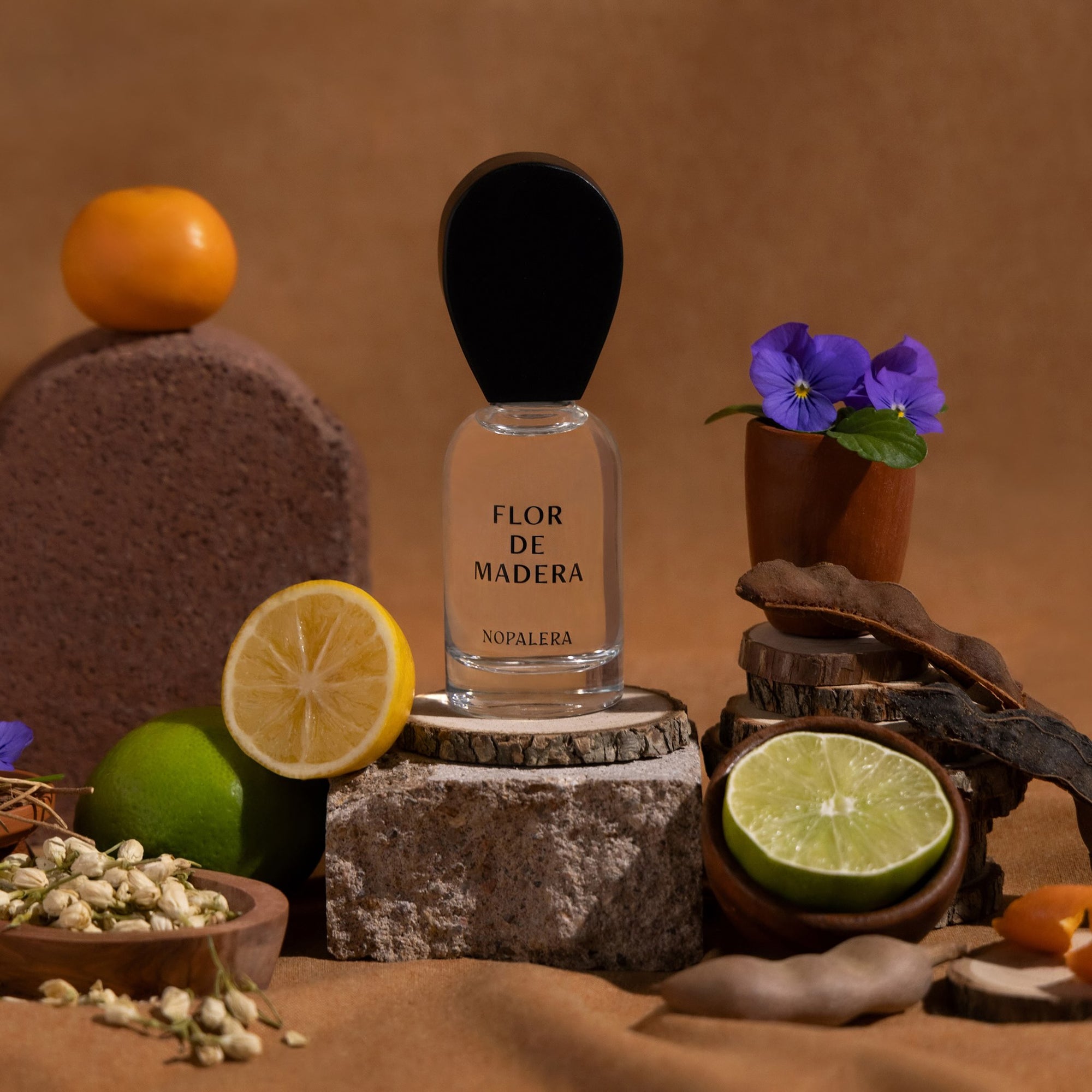 Nopalera Flor de Madera Luxury Mexican  perfume bottle surrounded by citrus fruits, flowers, and wood elements representing the fragrance notes