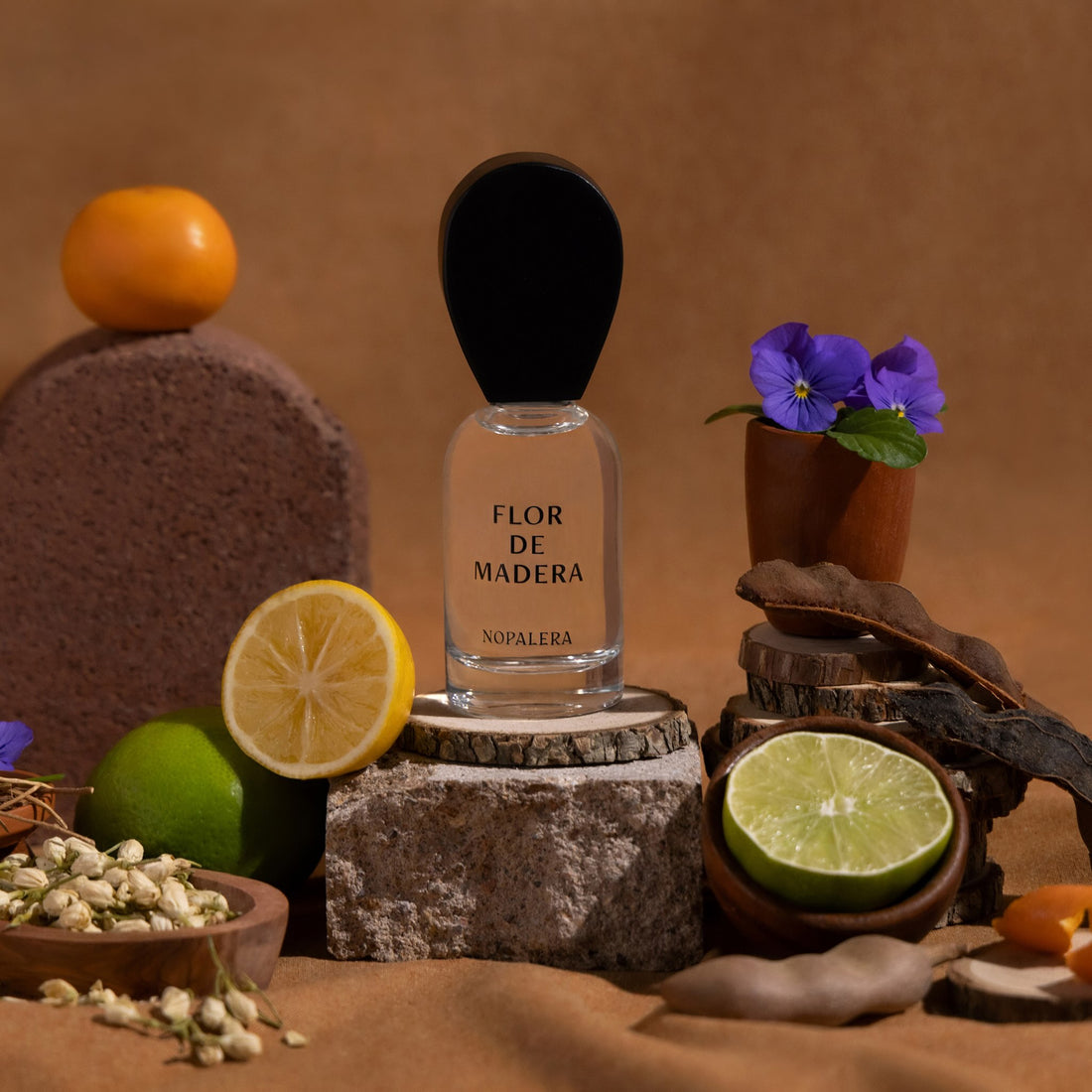 Nopalera Flor de Madera Luxury Mexican  perfume bottle surrounded by citrus fruits, flowers, and wood elements representing the fragrance notes