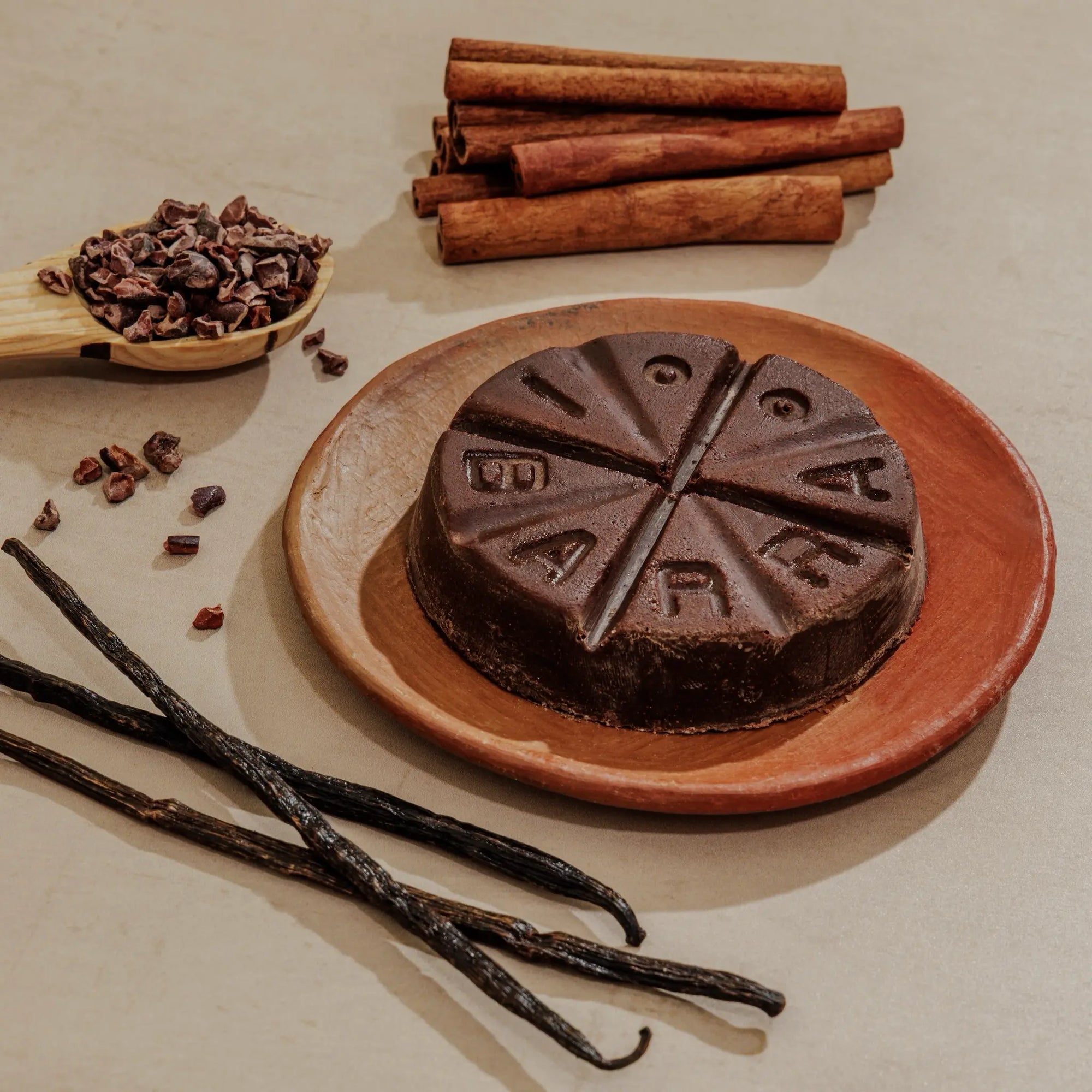 Chocolate cake with 'Fudgy' branding on a plate, surrounded by vanilla beans, cinnamon sticks, and cacao nibs.