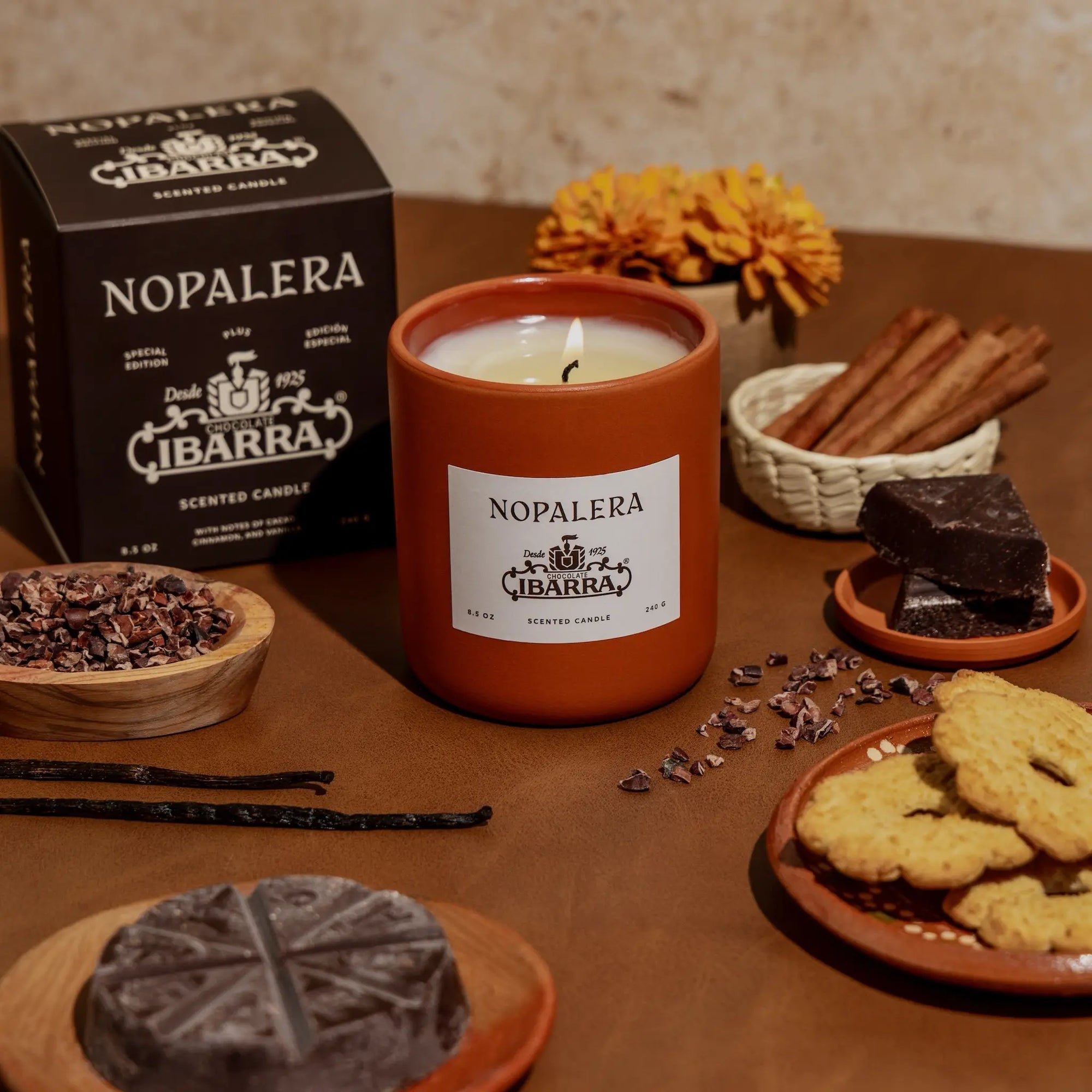 Nopalera Ibarra candle on a table with cookies, chocolate, and flowers