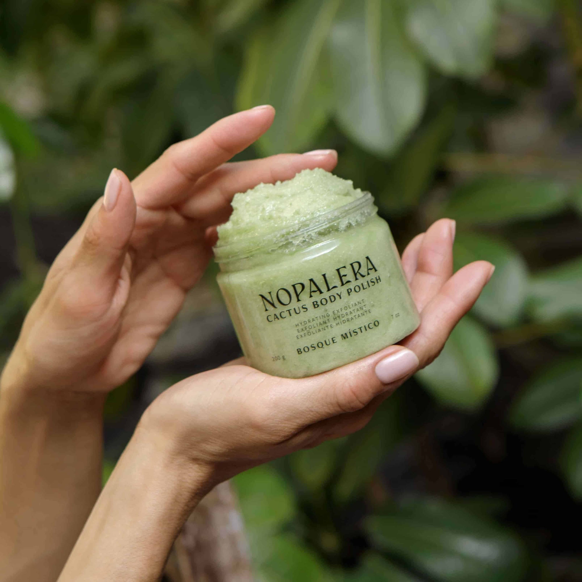 Person holding a jar of Nopalera Cactus Body Polish against a green leafy background