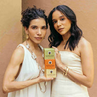 Two women holding Nopalera body polishes against a beige background