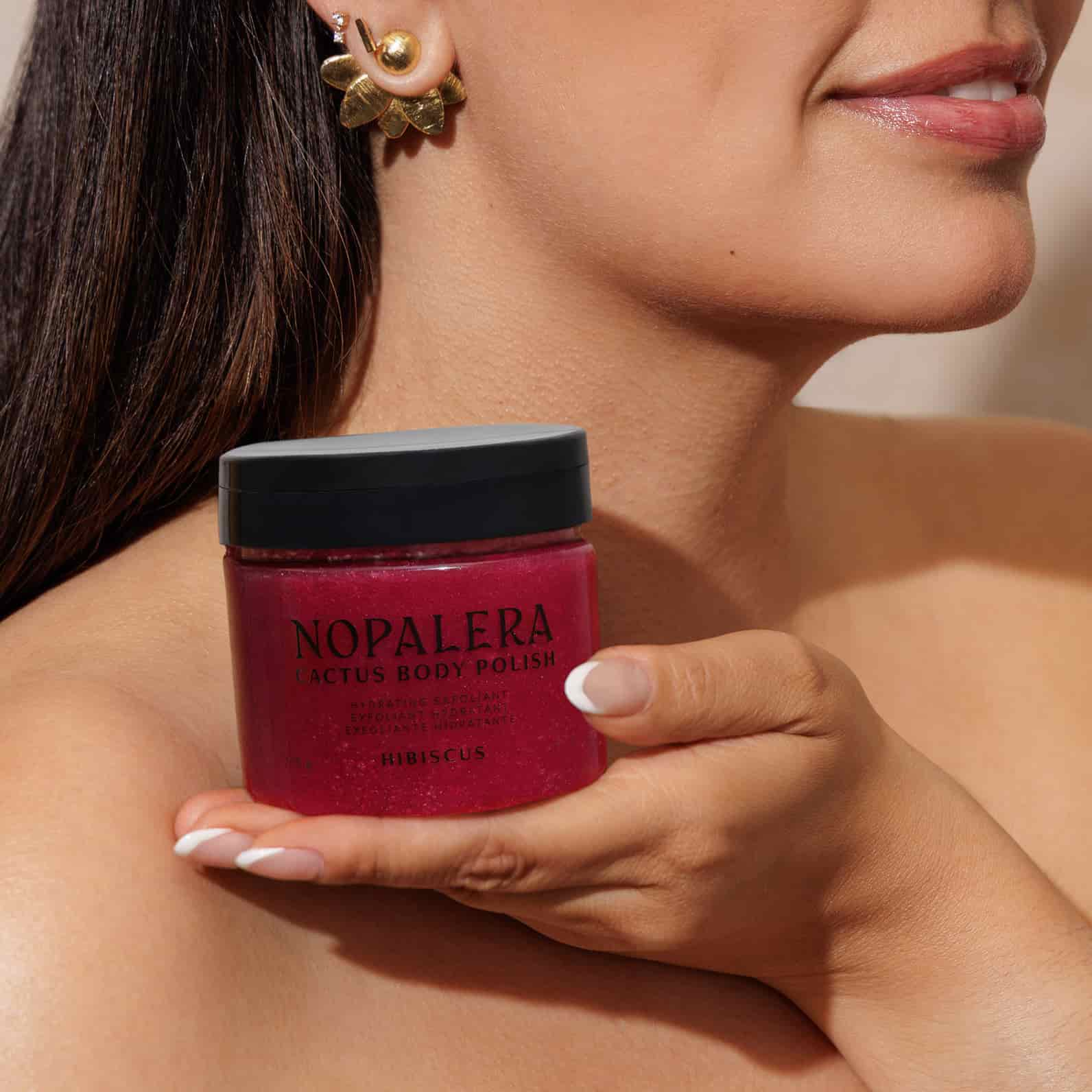 Woman holding a jar of Nopalera body polish hibiscus  against a neutral background