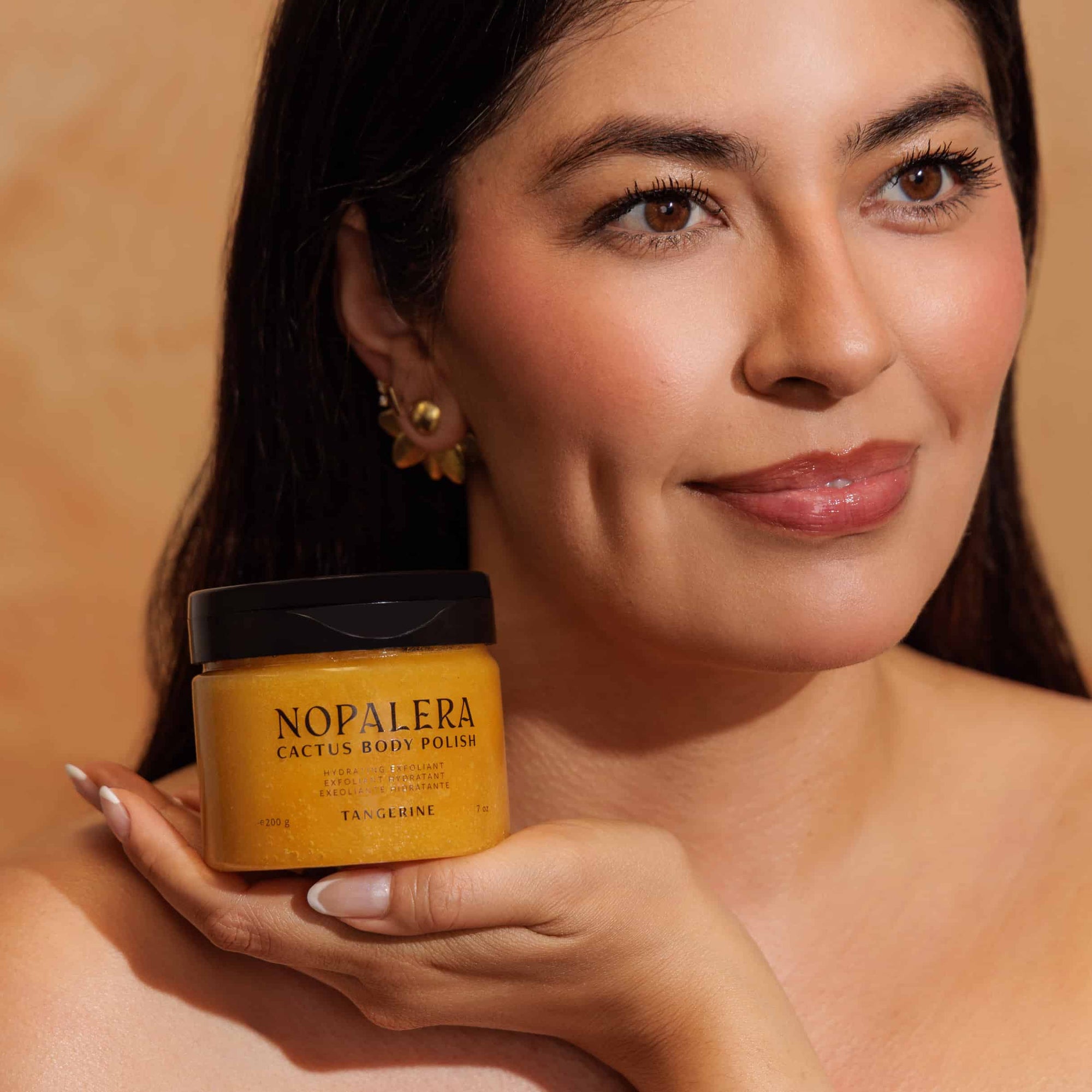 Woman holding a jar of Nopalera Cactus Body Polish  tangerine against an orange background