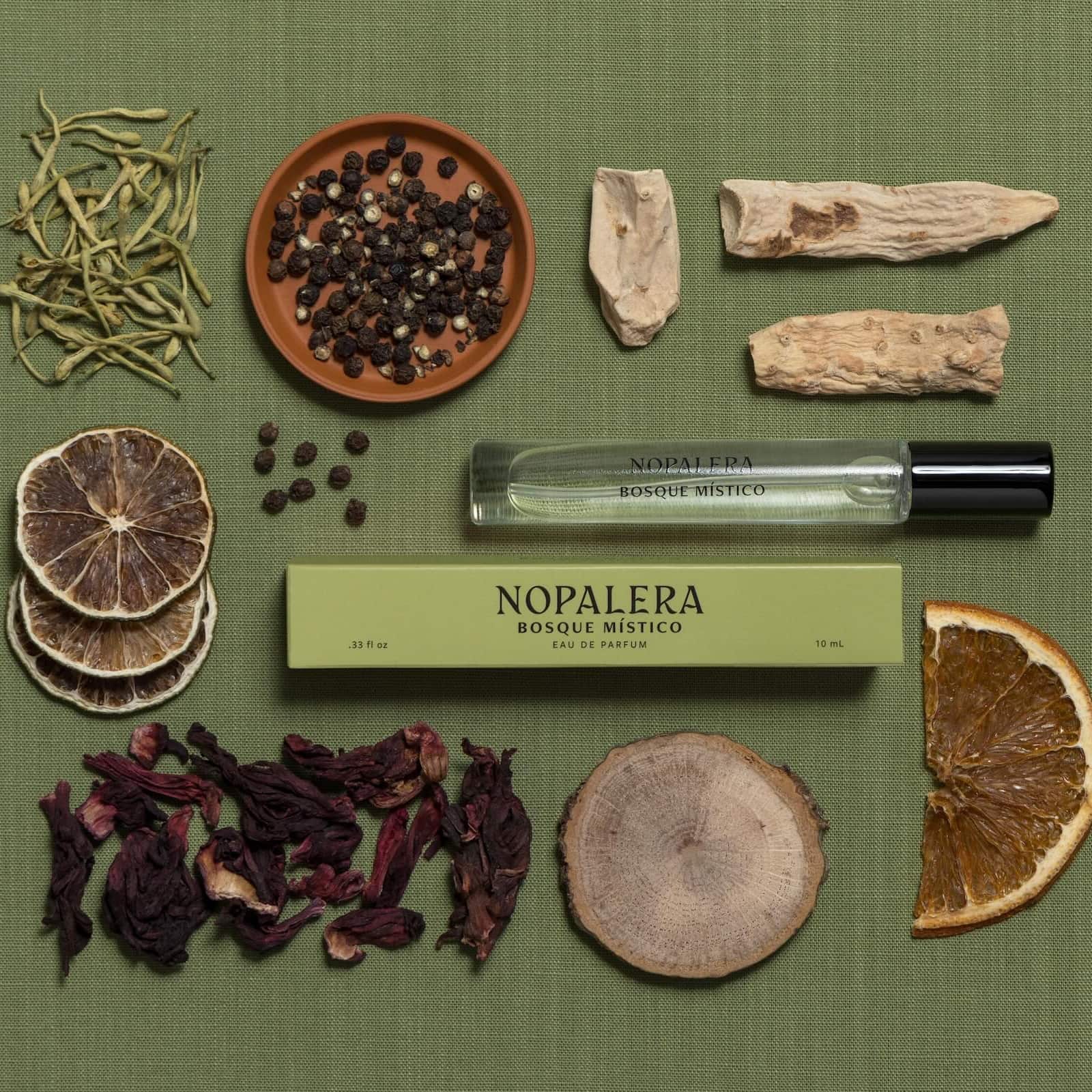 Luxury Mexican fragrance Nopalera Bosque Mistico perfume bottle surrounded by dried herbs and spices on a green background