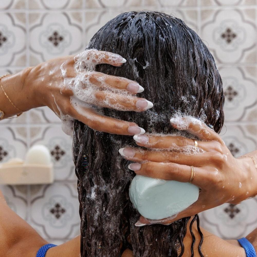 Hands holding Nopalera Moisturize and Shine shampoo bar in the shower