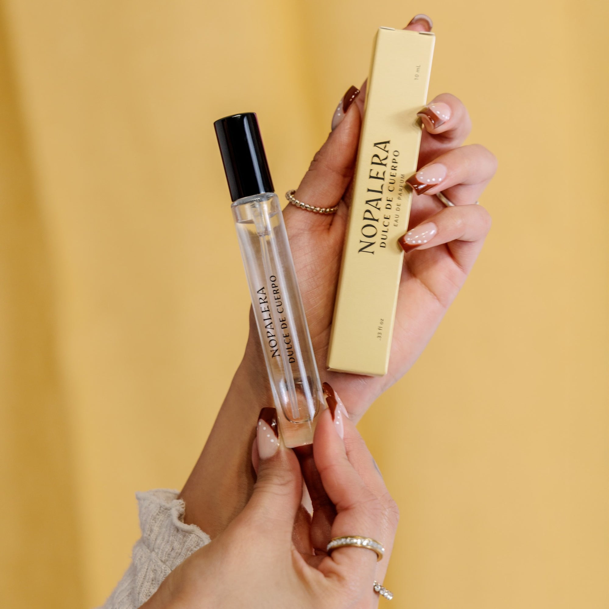 Hand holding Nopalera Luxury Mexican fragrance Dulce de Cuerpo travel perfume roller with product box on a yellow background