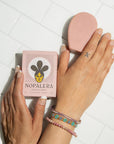 Hands holding Nopalera cactus soap beside a blush-toned beauty bar on white tile.