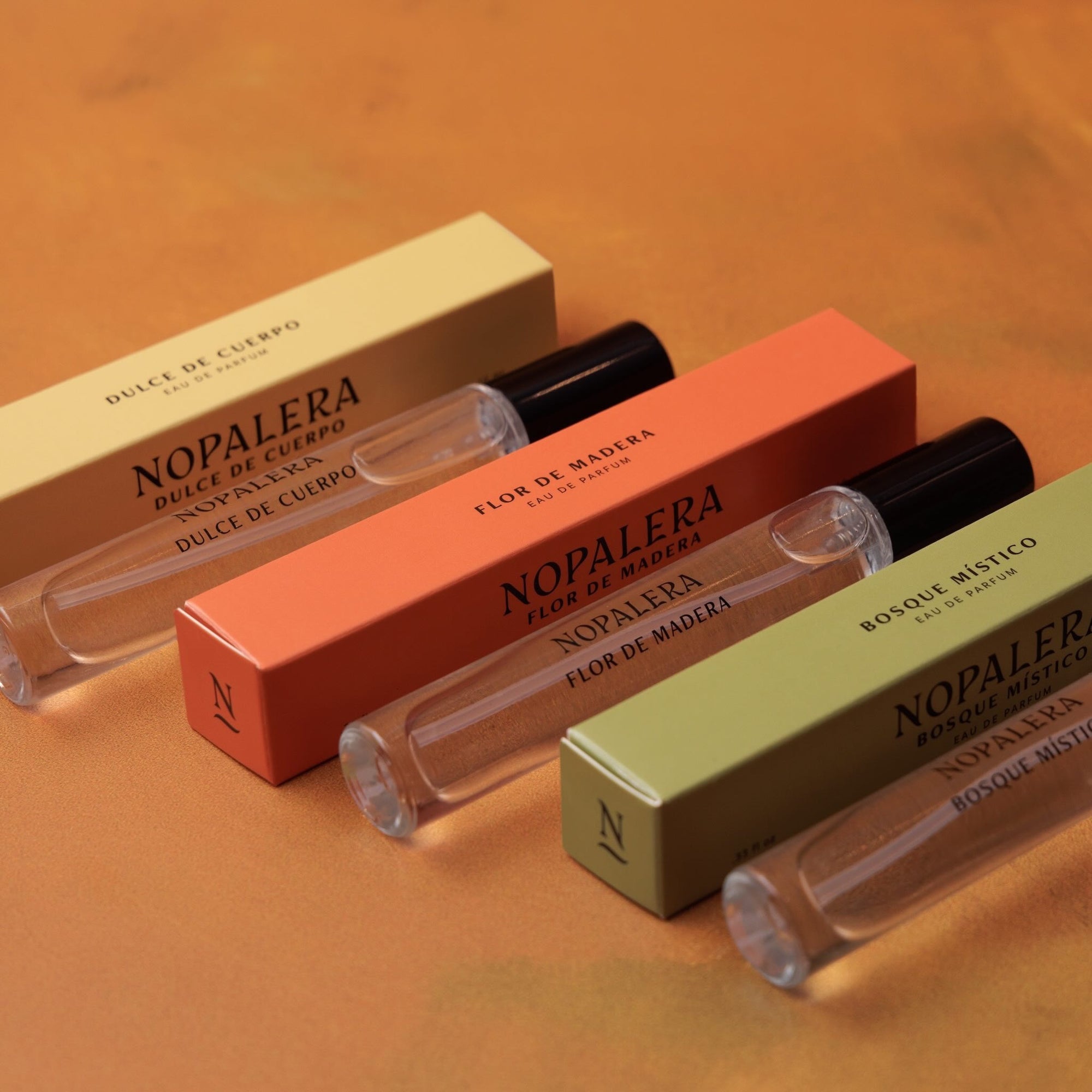 Nopalera travel perfume rollers in Dulce de Cuerpo, Flor de Madera, and Bosque Místico fragrances with matching packaging.