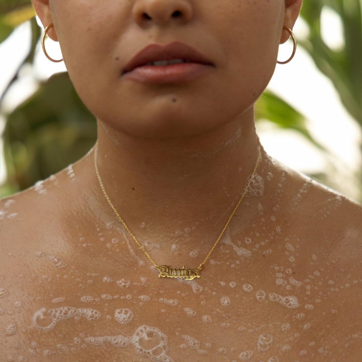 Close-up of glowing skin with soap bubbles and a gold necklace.