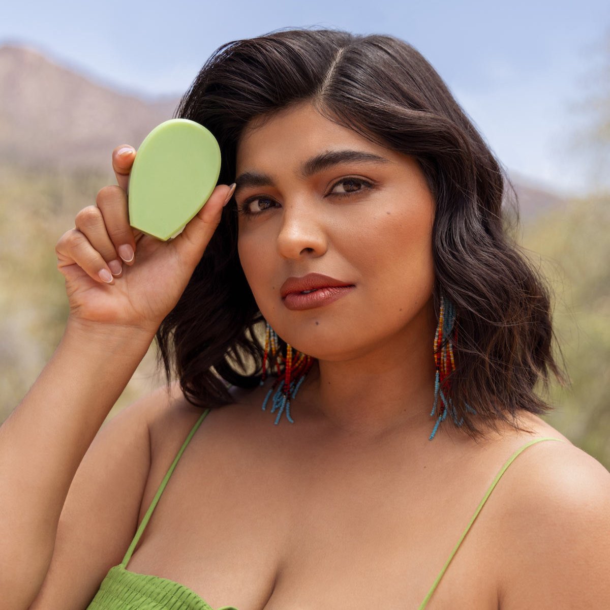 Model holding a green Nopalera beauty bar outdoors in a desert-inspired setting.