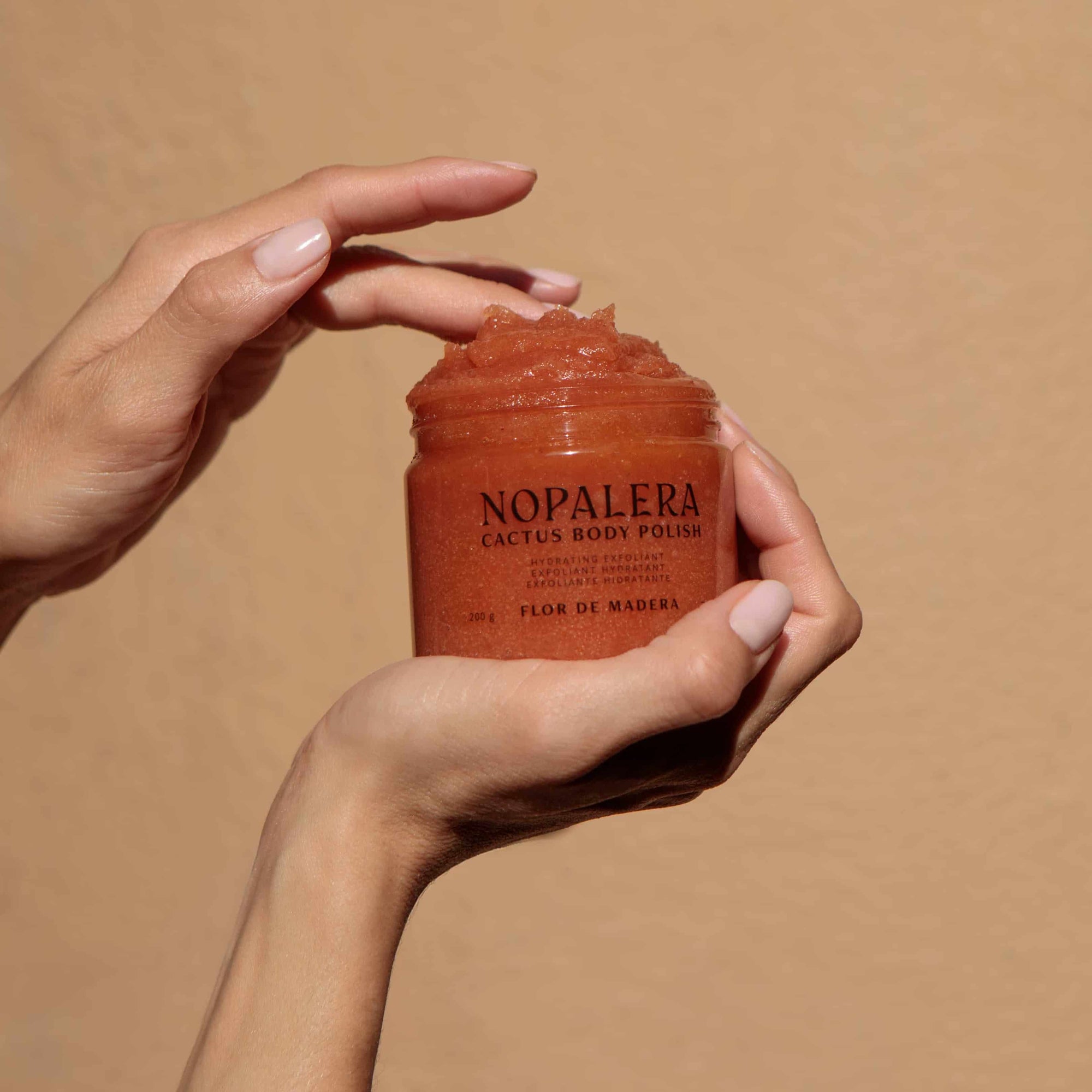 Hand holding a jar of Nopalera cactus body polish Flor de Madera against a beige background