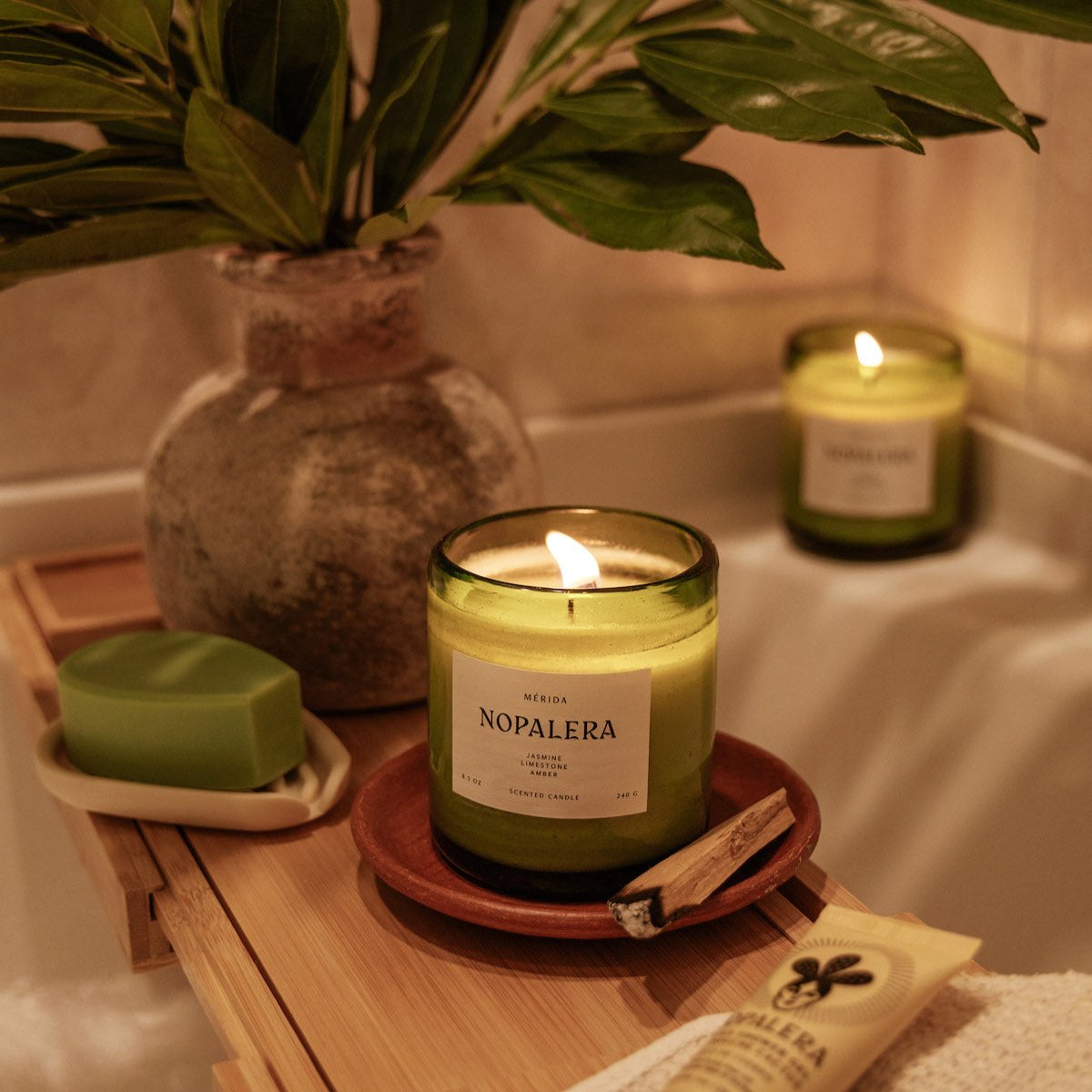 lit Nopalera Mérida scented candle in green glass jar on wooden bath tray
