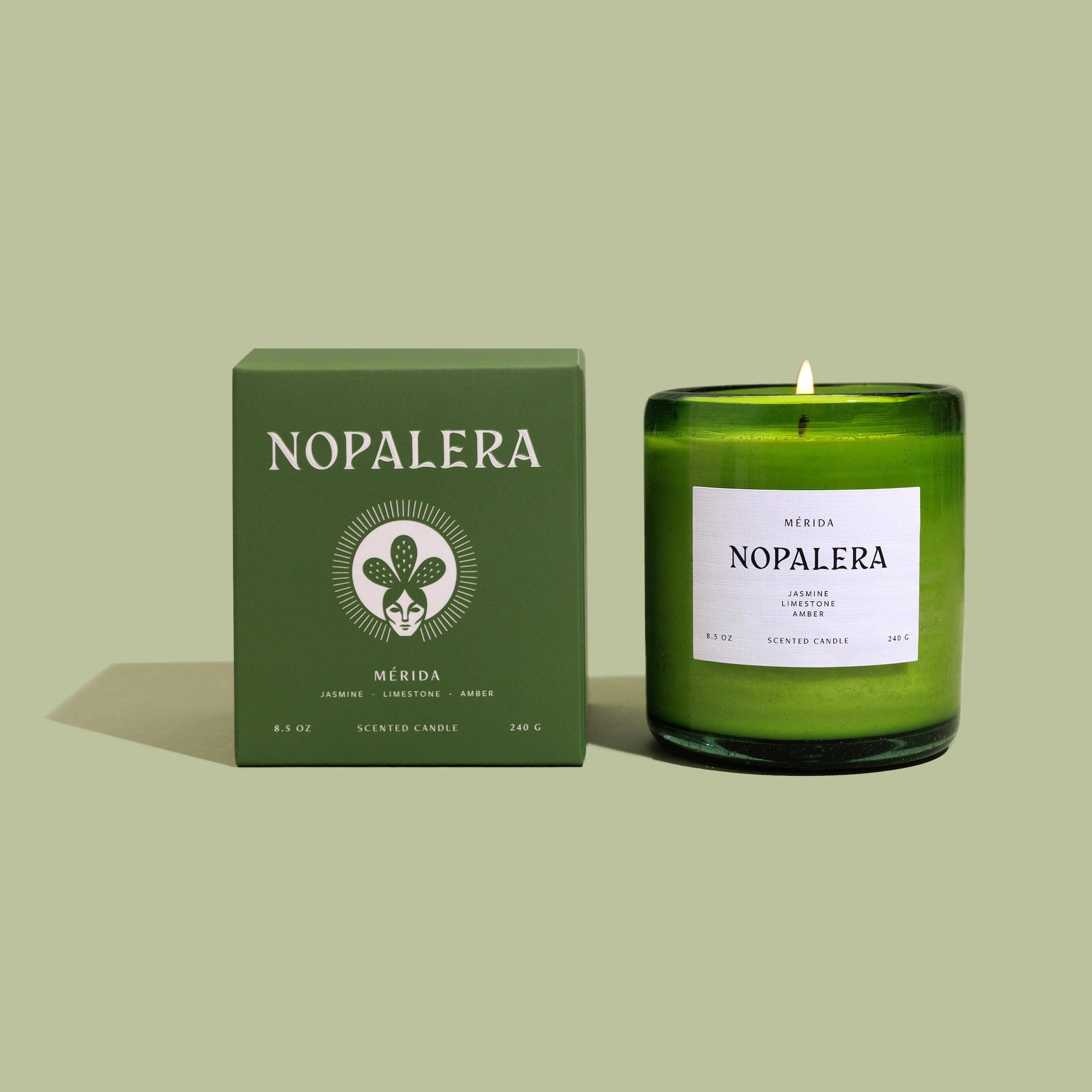A green glass Mérida candle with a lit wick, labeled 'Nopalera' next to a matching green box with the text 'Nopalera Merida' and the Yucatan flag emblem.