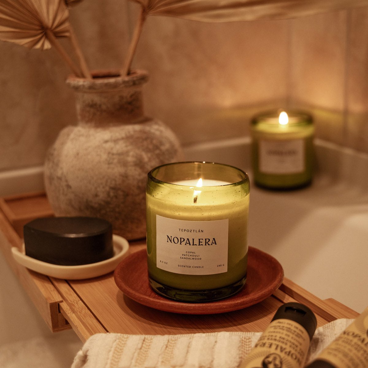 lit Nopalera scented Tepoztlan candle in green glass jar on wooden tray in bathroom