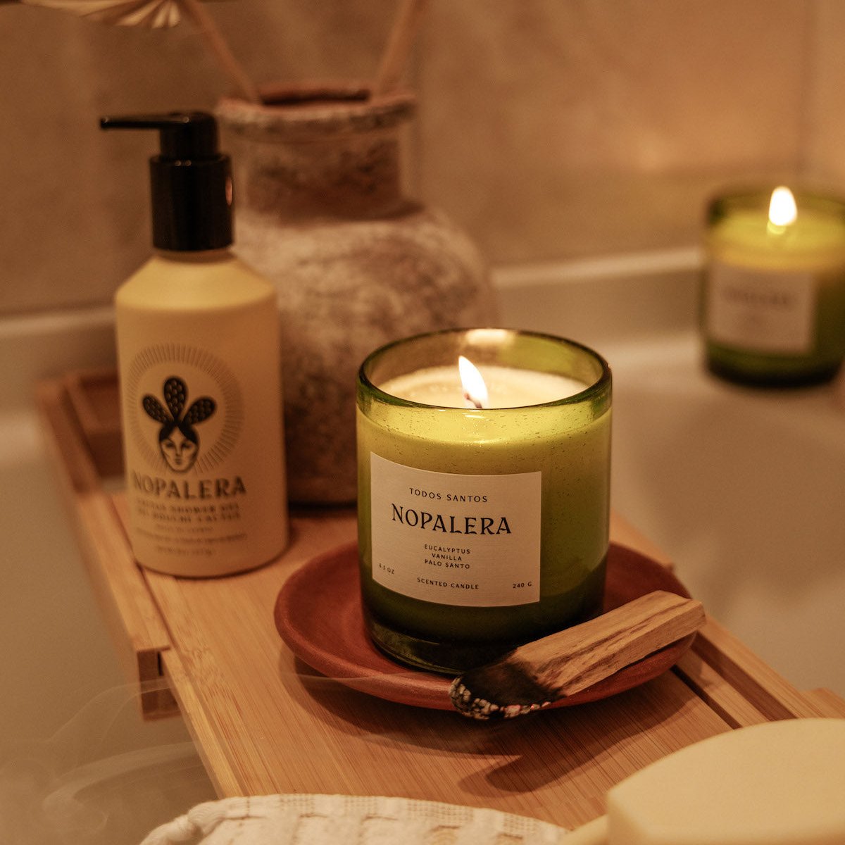 Nopalera Todos Santos scented candle lit in green glass jar on wooden bath tray